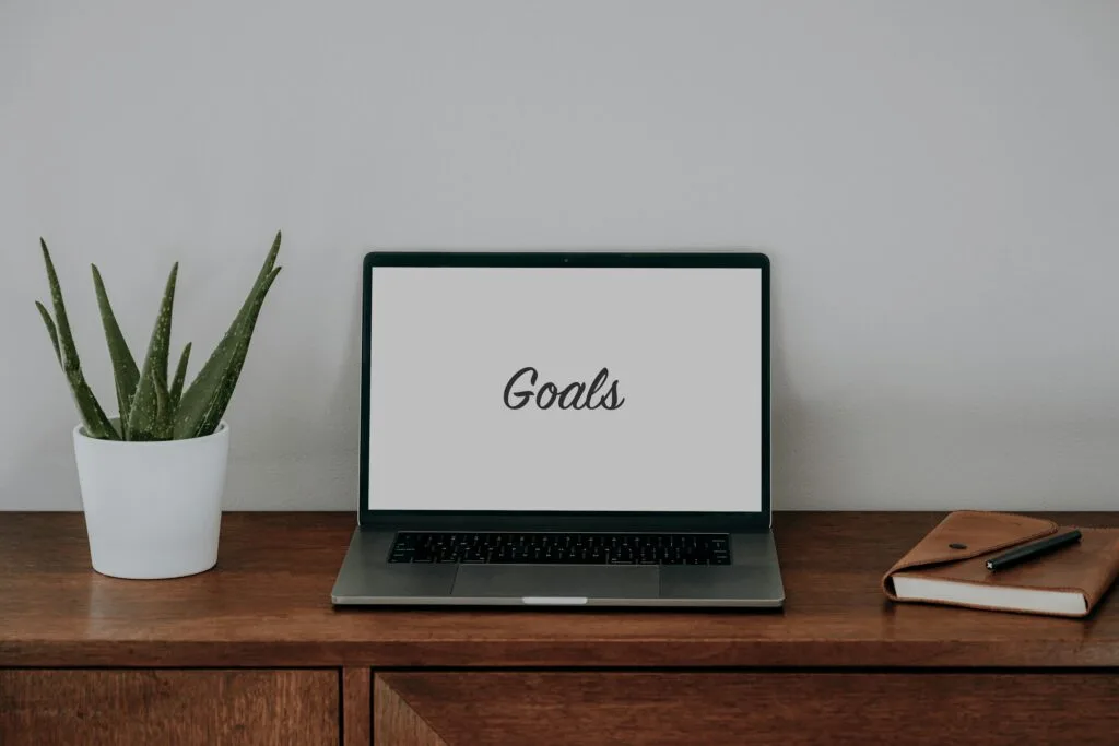 Minimal workspace with a laptop displaying the word “Goals,” representing how to prioritize your goals.
