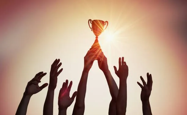 Silhouettes of a winning team raising a trophy at sunset, symbolizing a small victory and shared success.